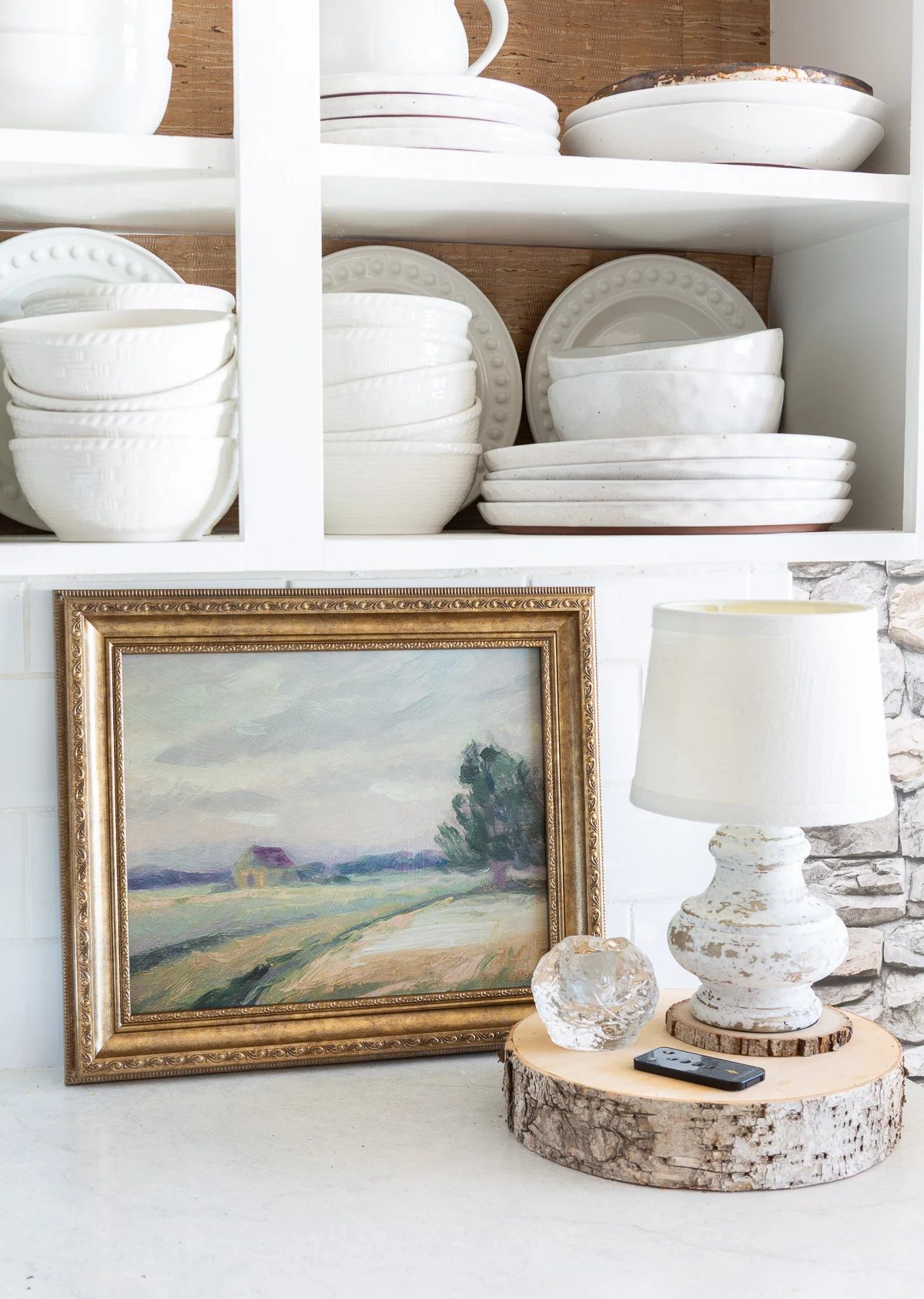 Looking at a kitchen counter where framed art is leaning against a white tile backsplash.