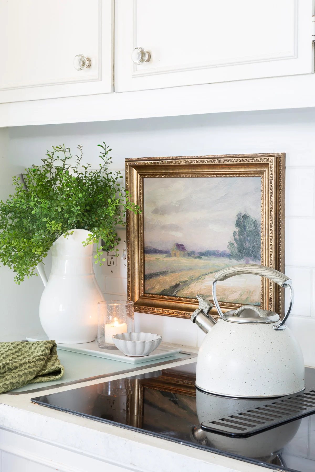 framed artwork hung on white tile backsplash in kitchen. Stove and teapot nearby.