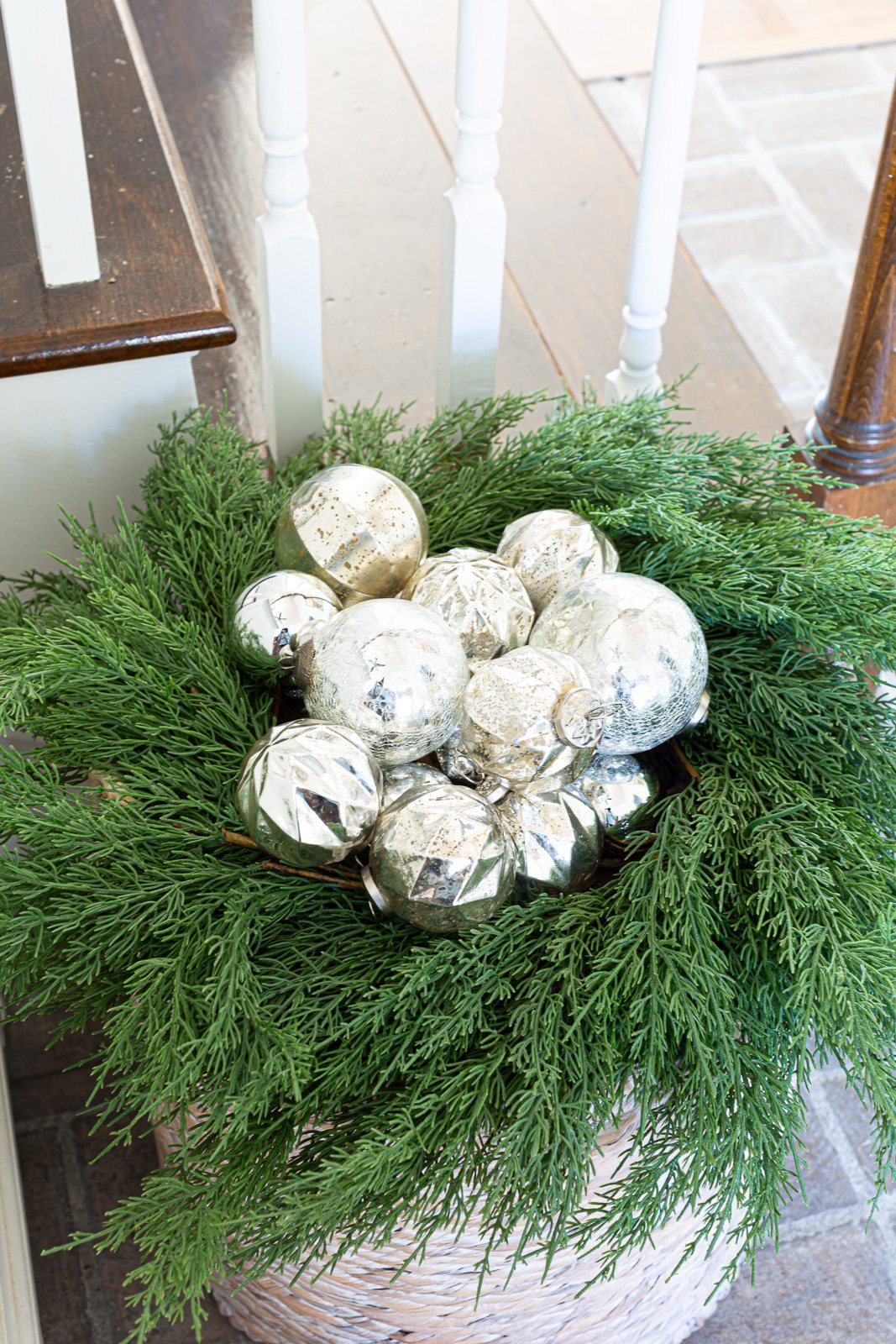 silver Christmas ornaments placed in the center of a greenery wreath on top of a floor basket.