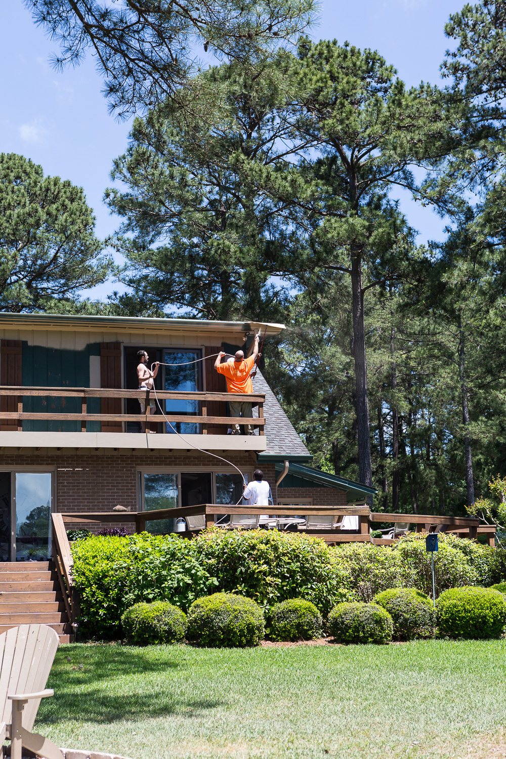 Two painters using a paint sprayer to paint a gutter and eave
