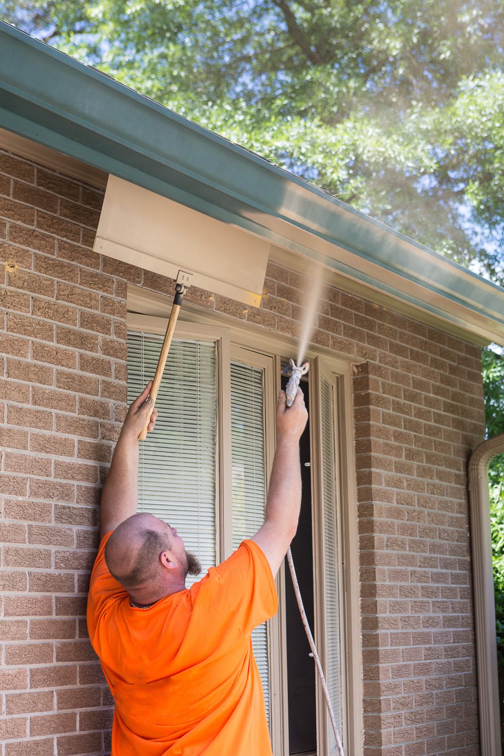 Using a paint shield to spray paint on the exterior of a home