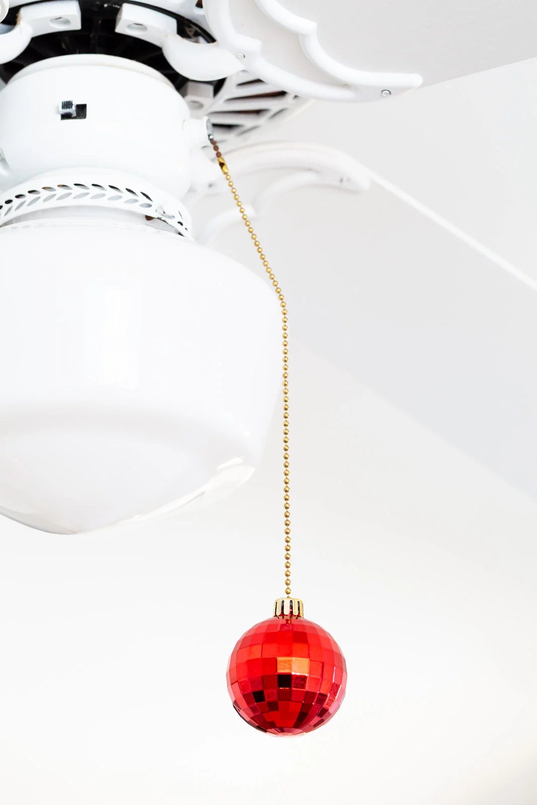 a red Christmas ornament added to the pull chain of a ceiling fan.
