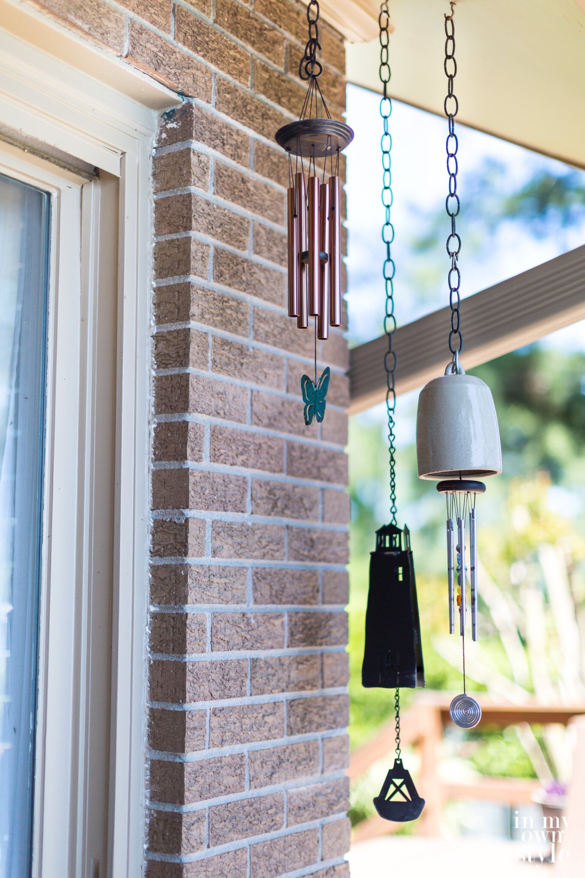 3 wind chimes hanging from a roof along a deck.