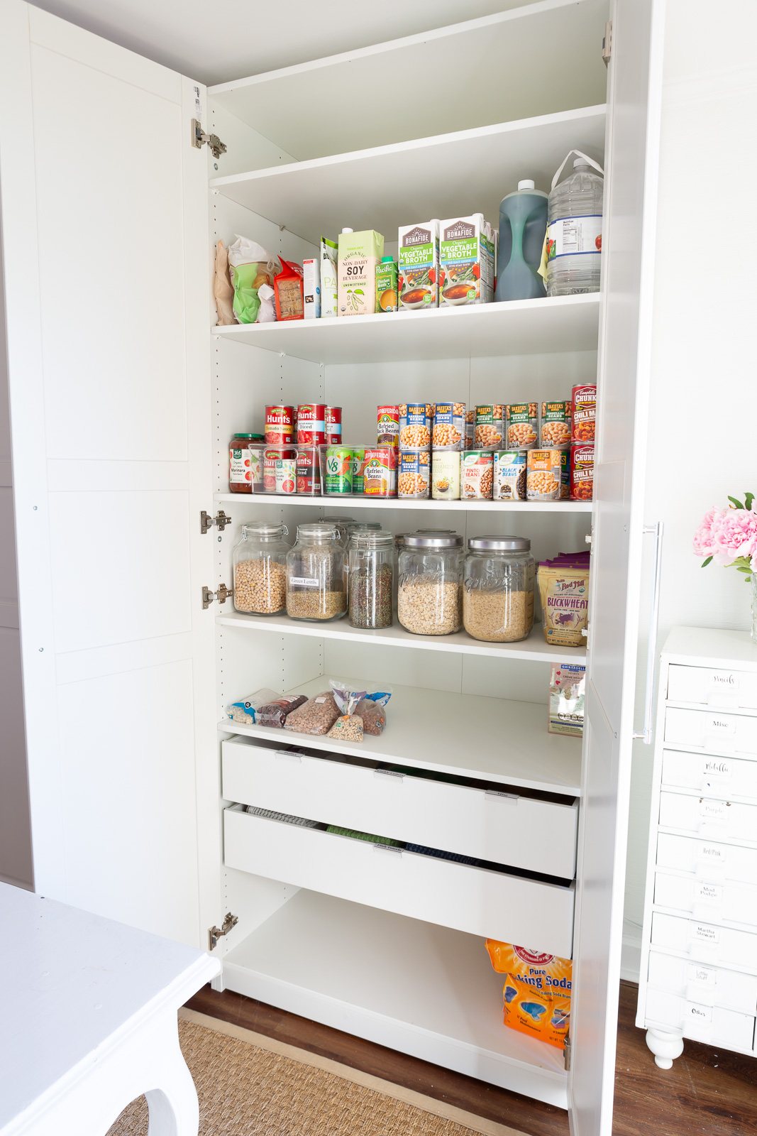 IKEA PAX storage closet in white fitted with shelves and 2 drawers to hold food and pantry staples in a multi-purpose room in a home.