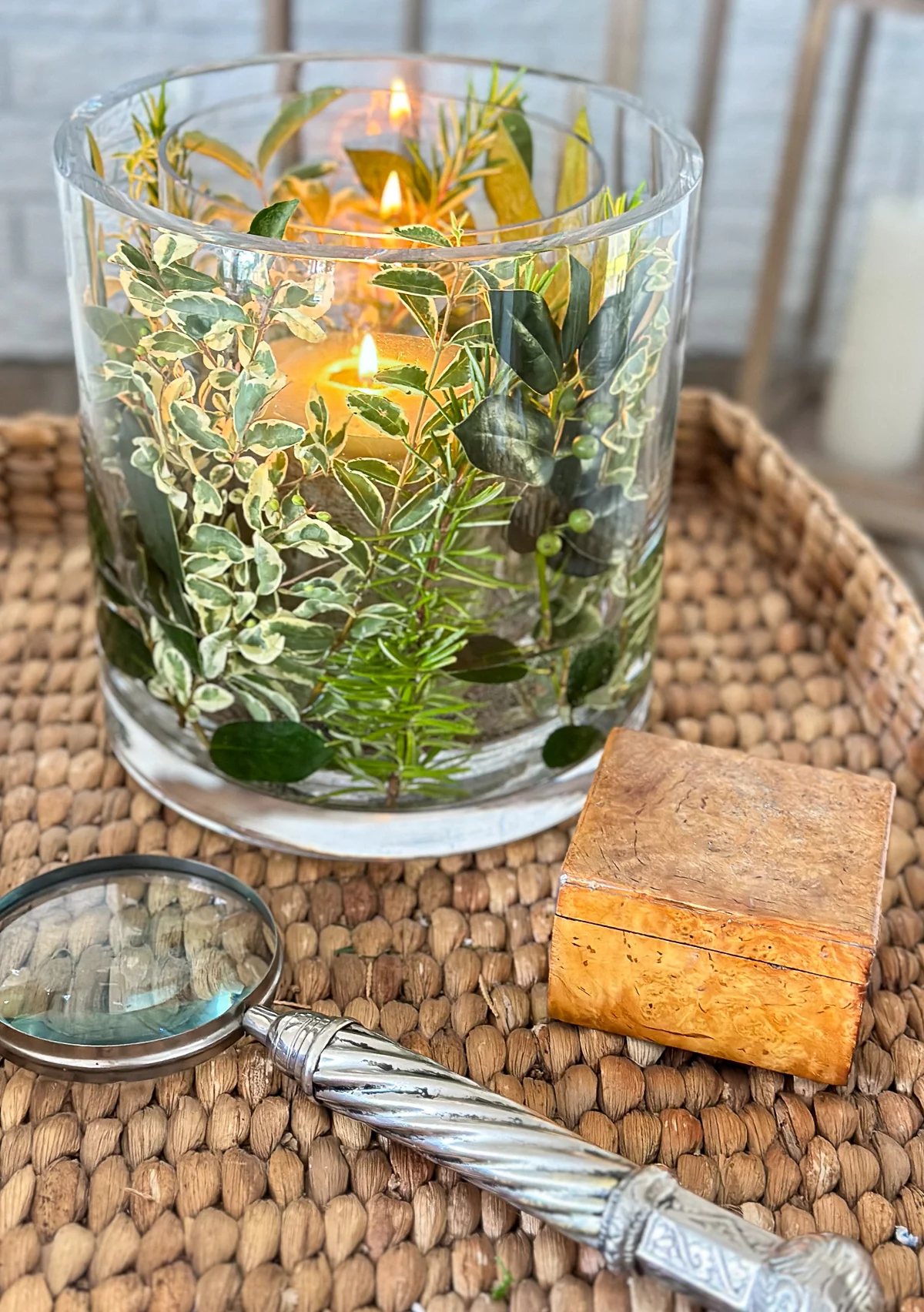 Close up of fresh herb and greenery DIY candle vase on a wicker tray table in a living room.