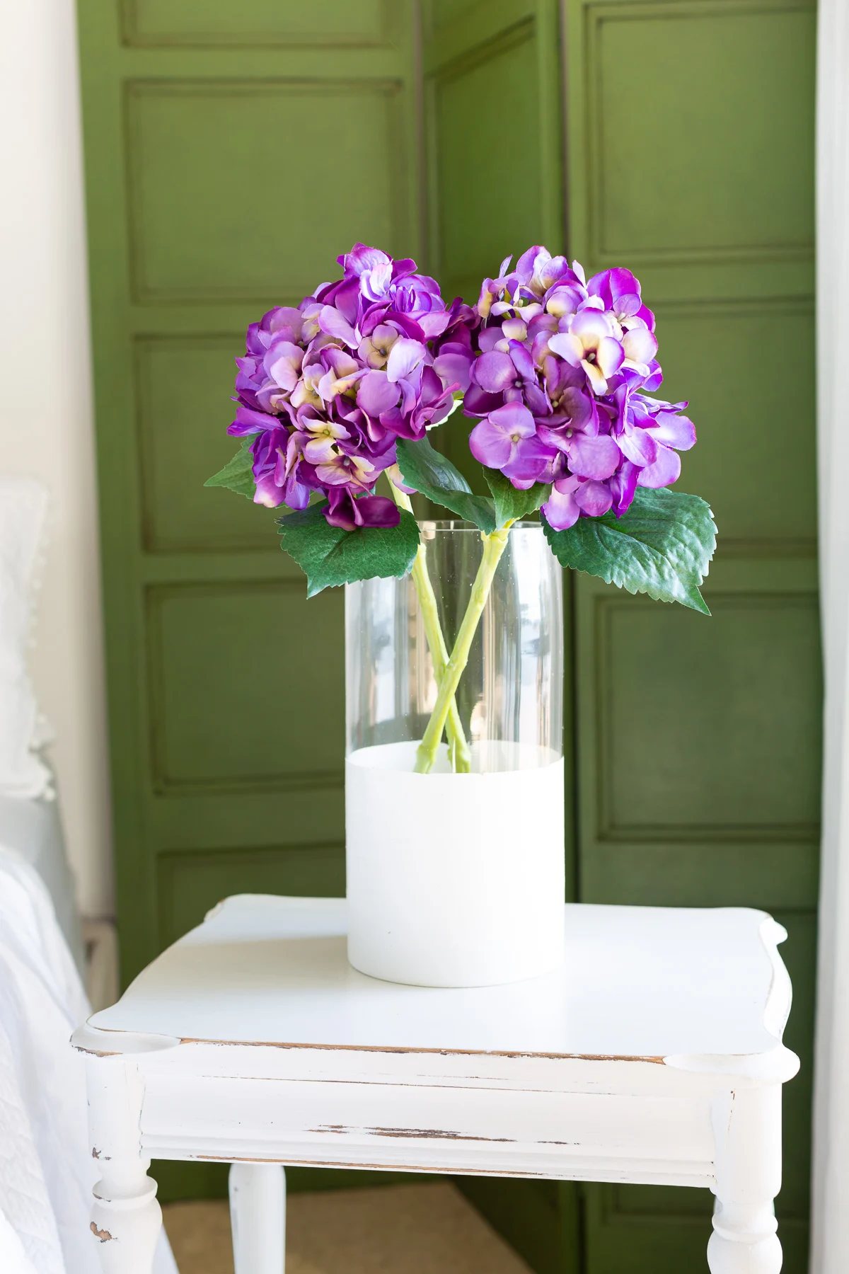 clear glass vase with bottom half painted white. Purple flowers in vase.