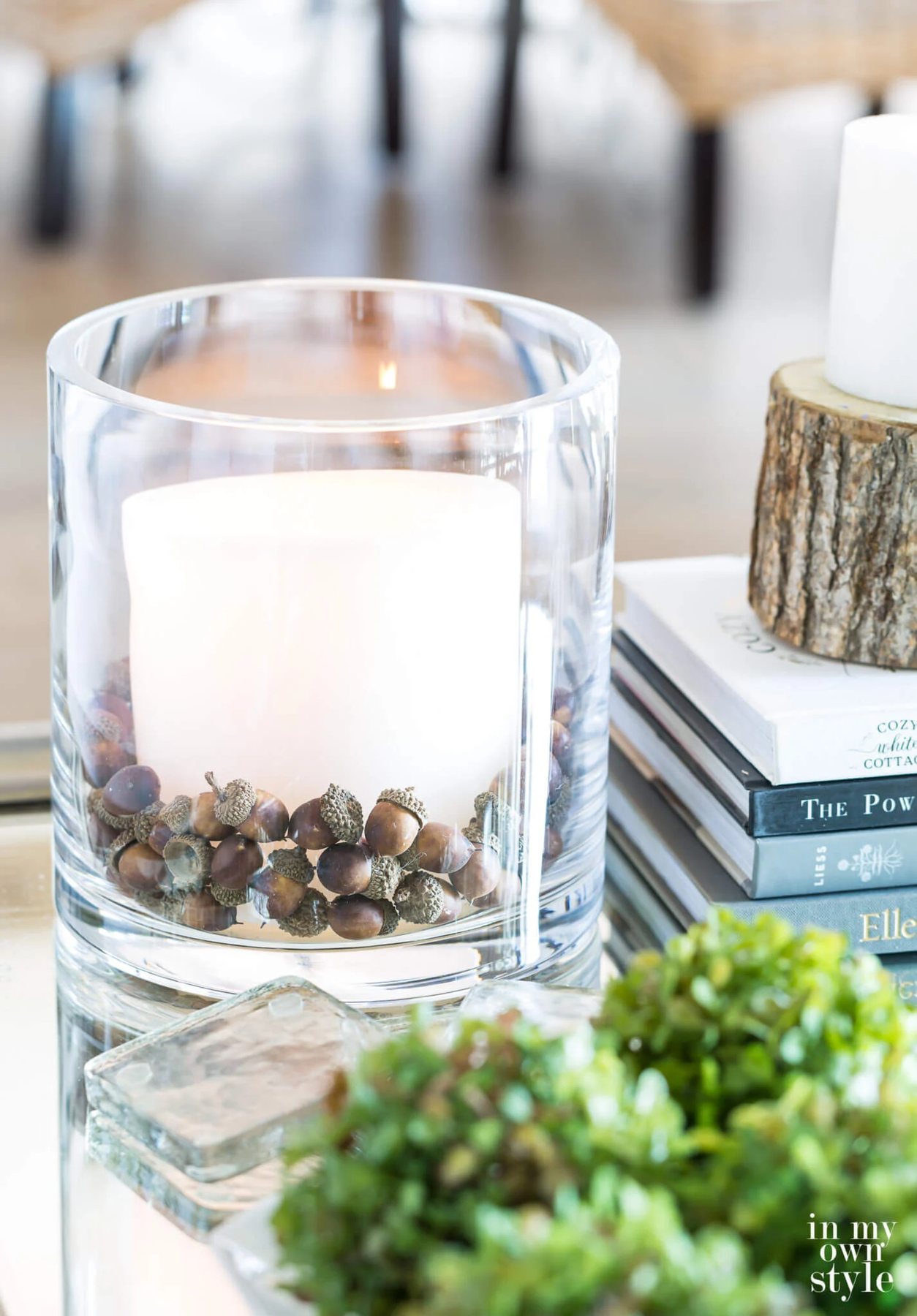 Pottery Barn glass cylinder vase filled with acorns and large white candle on a coffee table.