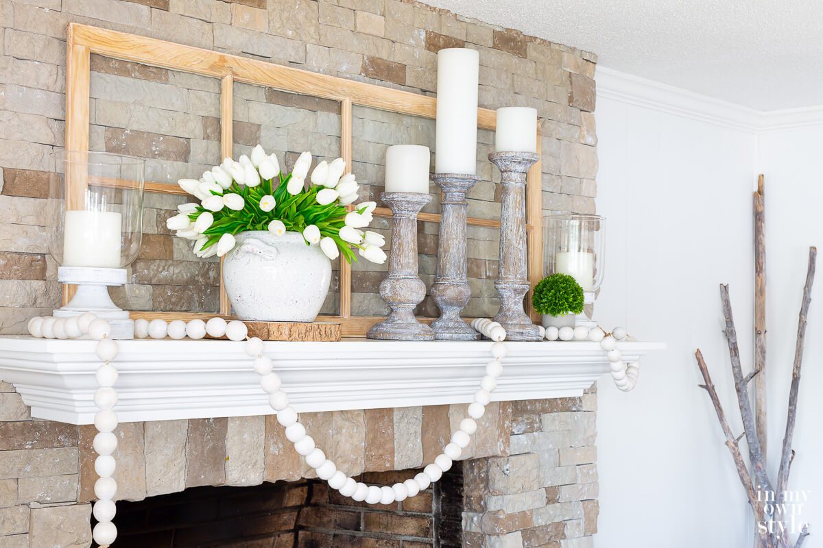 White and green summer themed mantel decor on a stone fireplace.