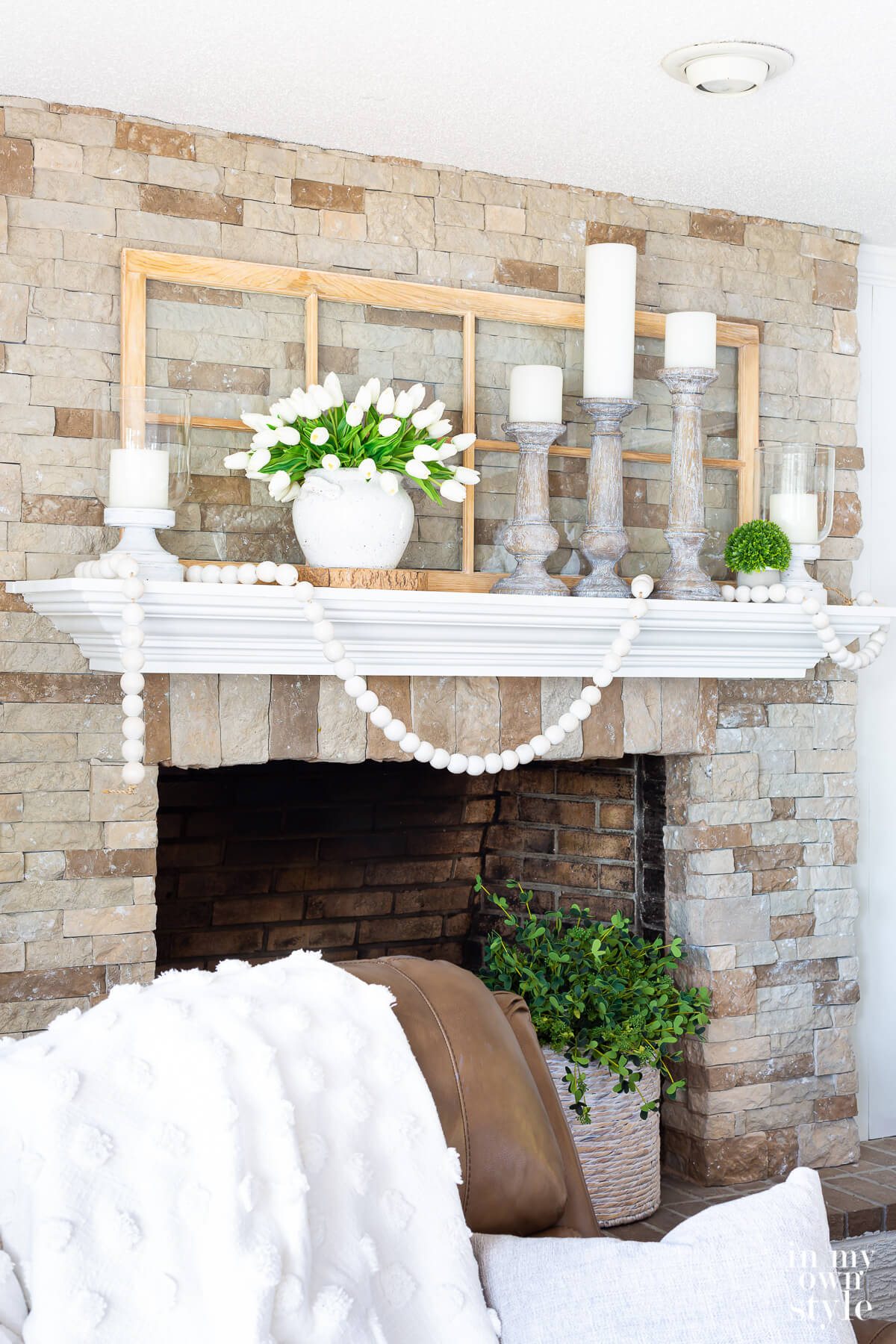 White and green summer themed mantel decor on a stone fireplace.