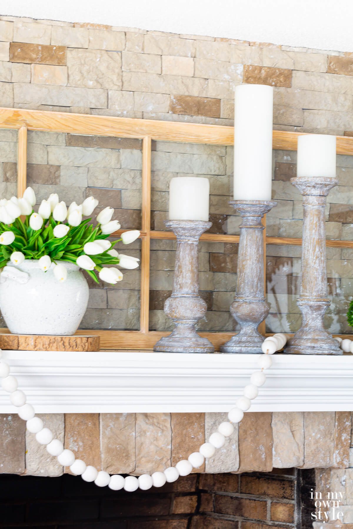 3 large white-washed wood candle holders with white pillar candles decorating a fireplace mantel.