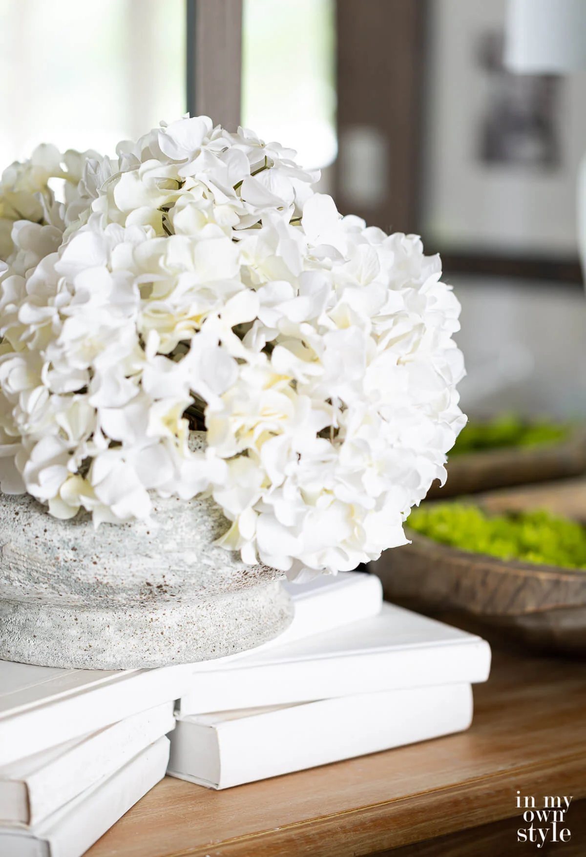 White hydrangeas on a stack of white books on a table in front of a wall of mirrors.