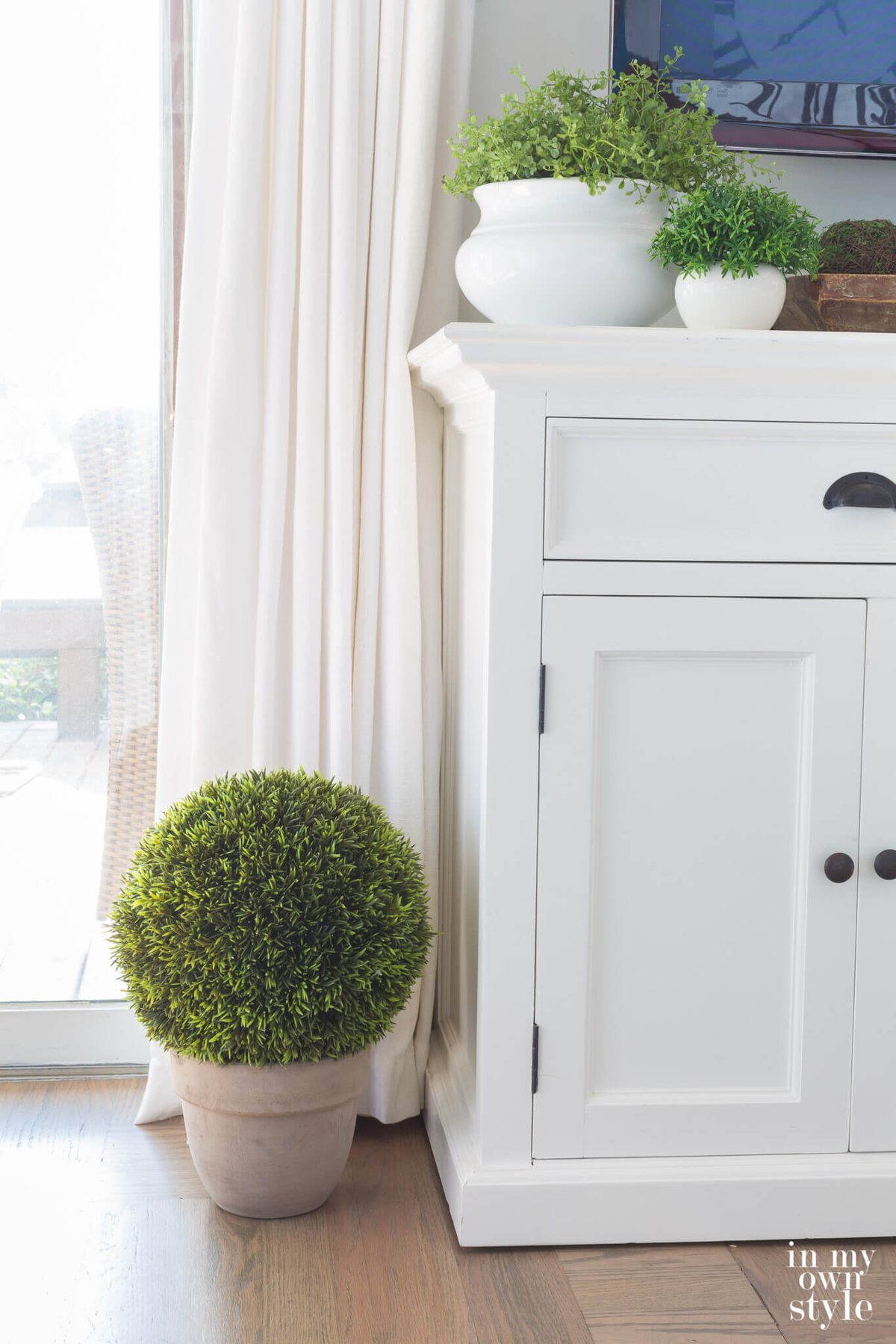 Green moss globe on floor in whitewashed terracotta pot.
