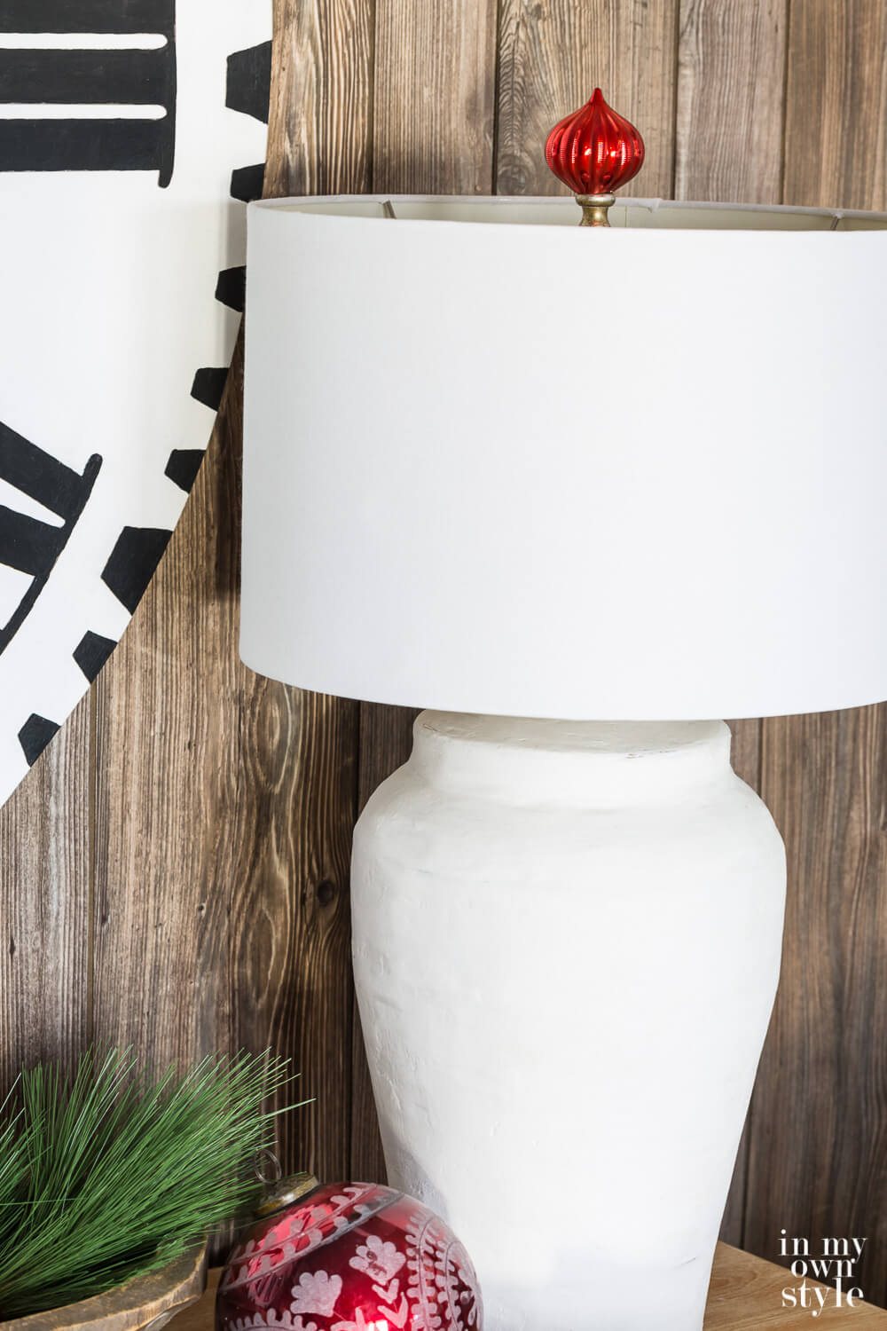 Holiday lamp finial idea. Close up of white table lamp with red Christmas ball ornament made into a finial above the lamp shade.