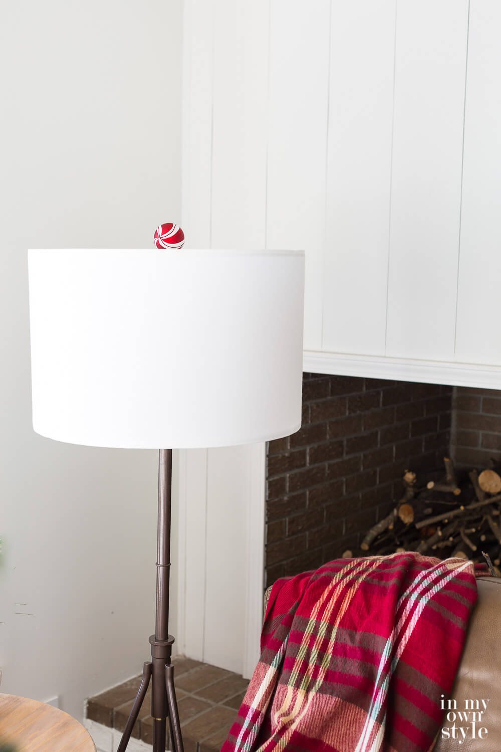 Bronze floor lamp with white drum shade with a red and white Christmas ornament finial.