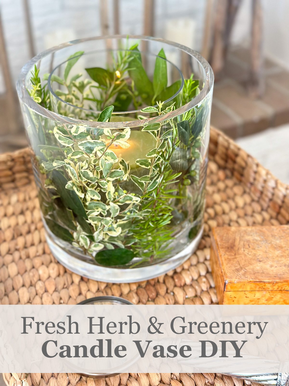 Fresh herb and greenery DIY candle vase on a wicker tray table in a living room.