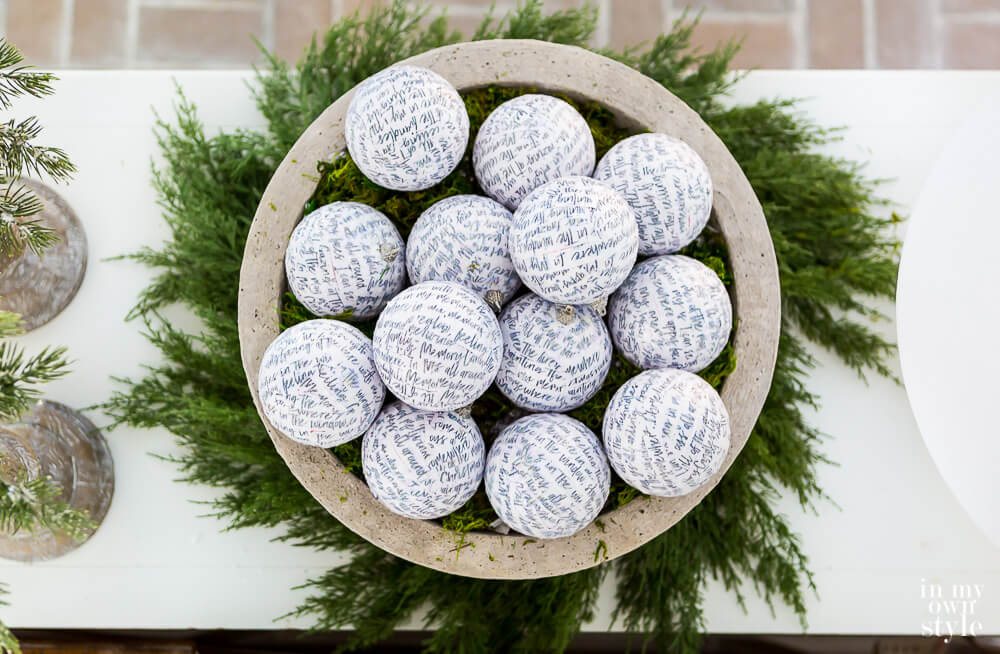 Large fake concrete planter DIY filled with white ornaments with black script. Cedar wreath underneath
