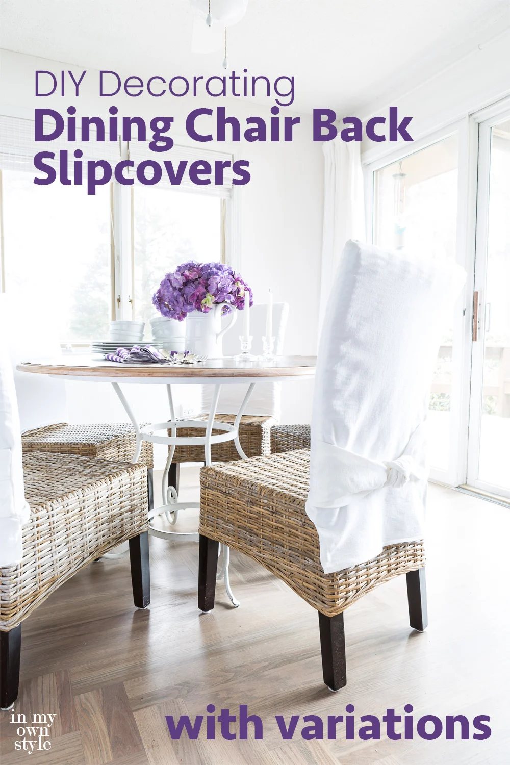 Casual dining area in a home with table and chairs. Chairs are wicker and have white chair back slipcovers on them. A white pitcher on the table has purple hydrangeas in it.