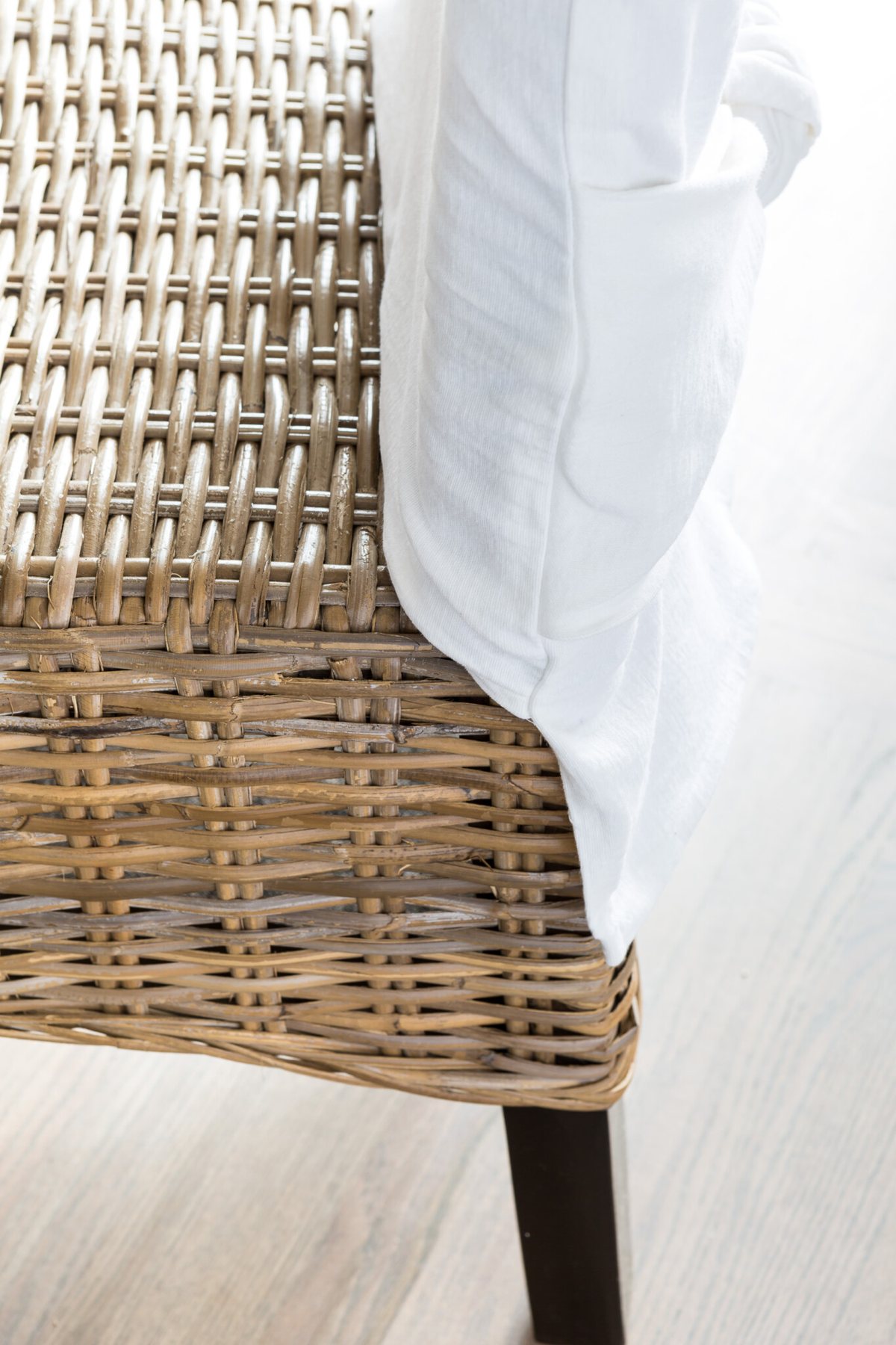 Close up of side view of a wicker dining with a white chair back slipcover on it..