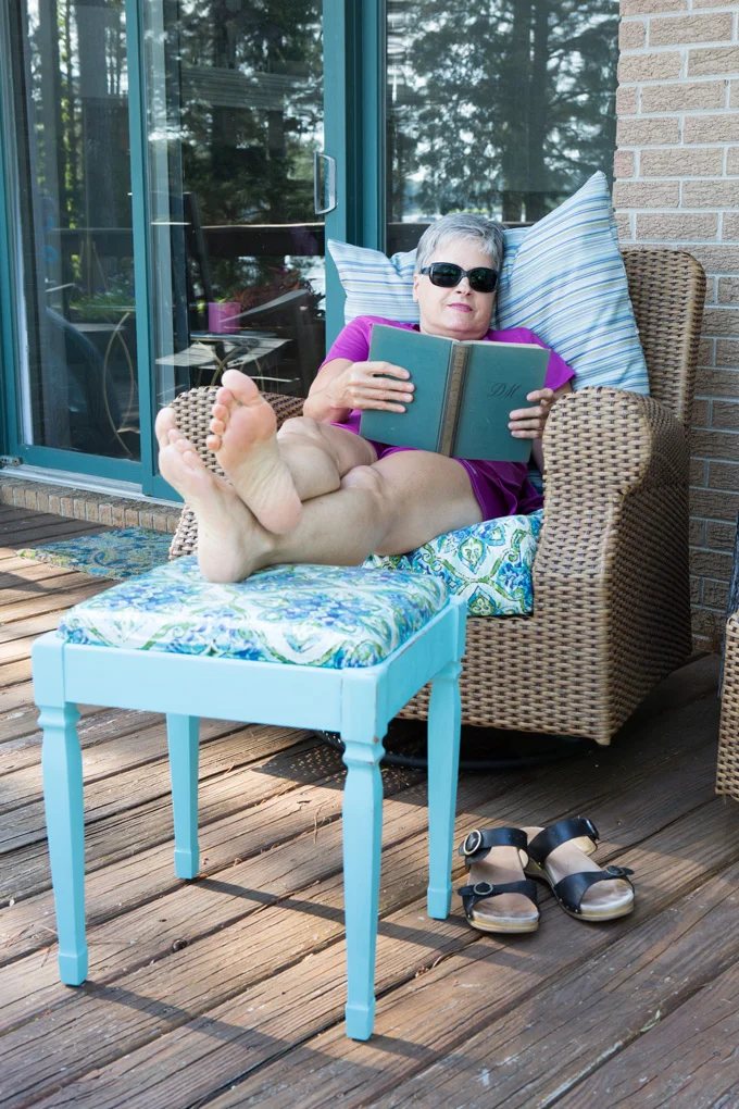 Blogger Diane sitting in chair reading a book with feet up on finished stool.