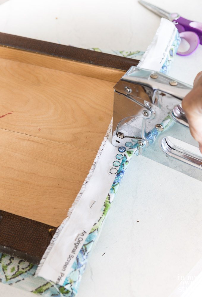 Using a staple gun to attach fabric to stool's removable top.