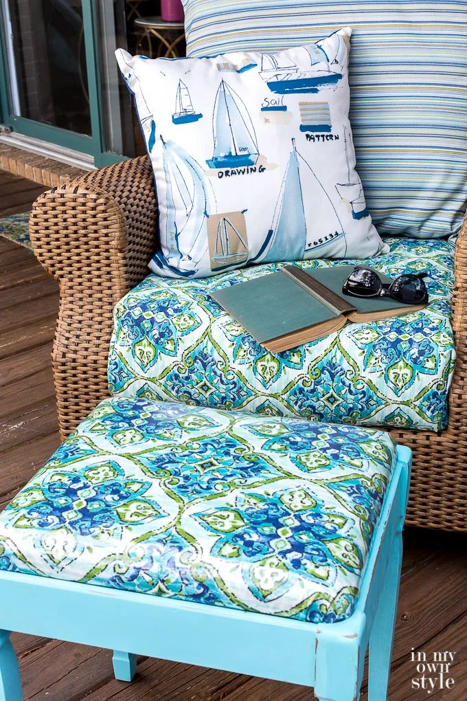 Close up of newly covered stool next to rattan rocker. The fabric on the stool matches the cushion on the rocker.