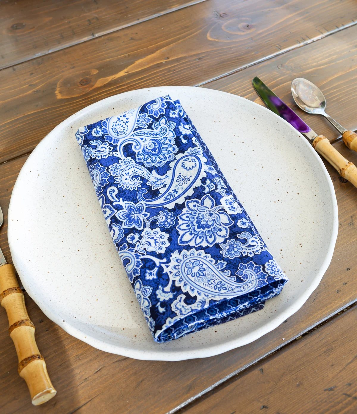 A paisley blue and white cloth napkin folded into a rectangle shape placed on a dinner plate.