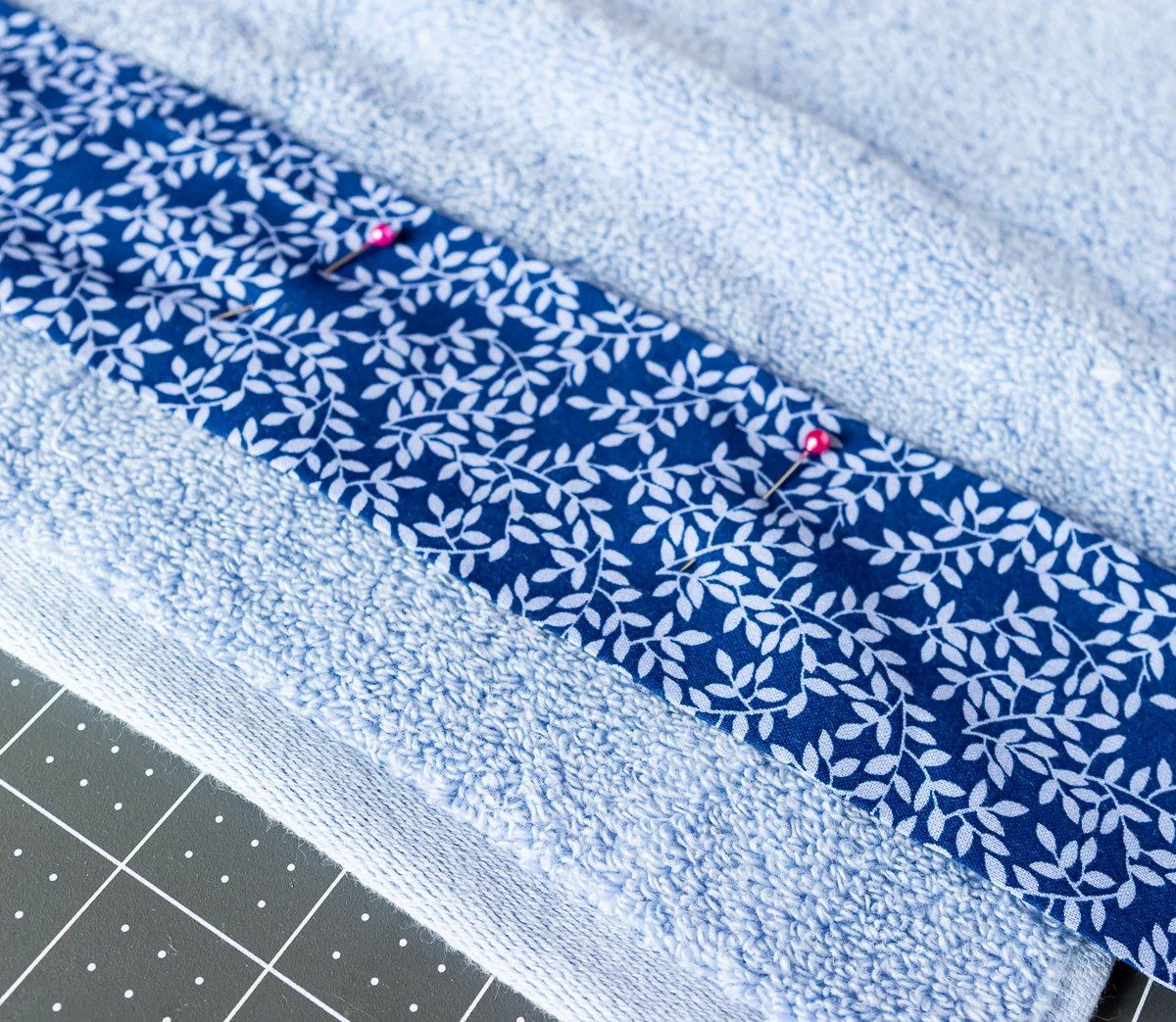 blue fabric being pinned to a bath towel before sewing it on.