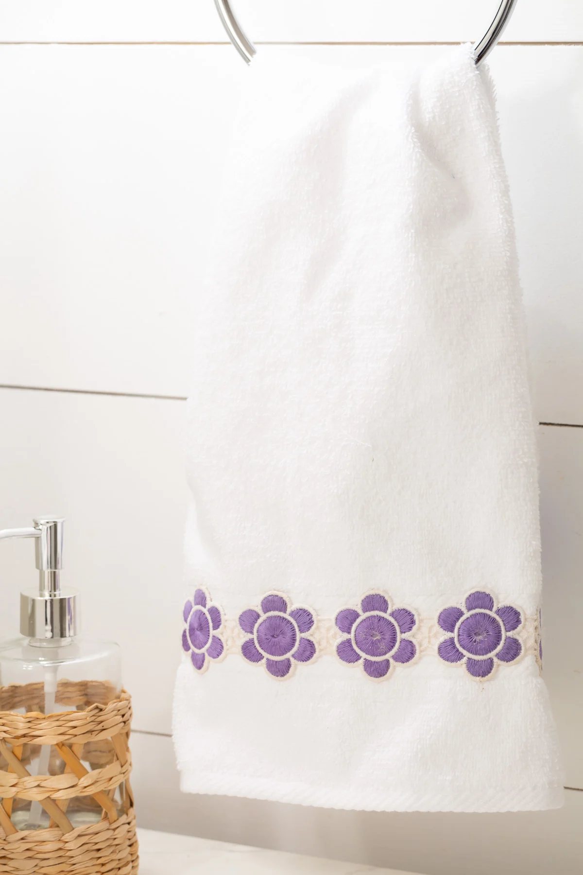 vintage purple and white flower ribbon sewn onto a hand towel hanging from towel ring in a bathroom.