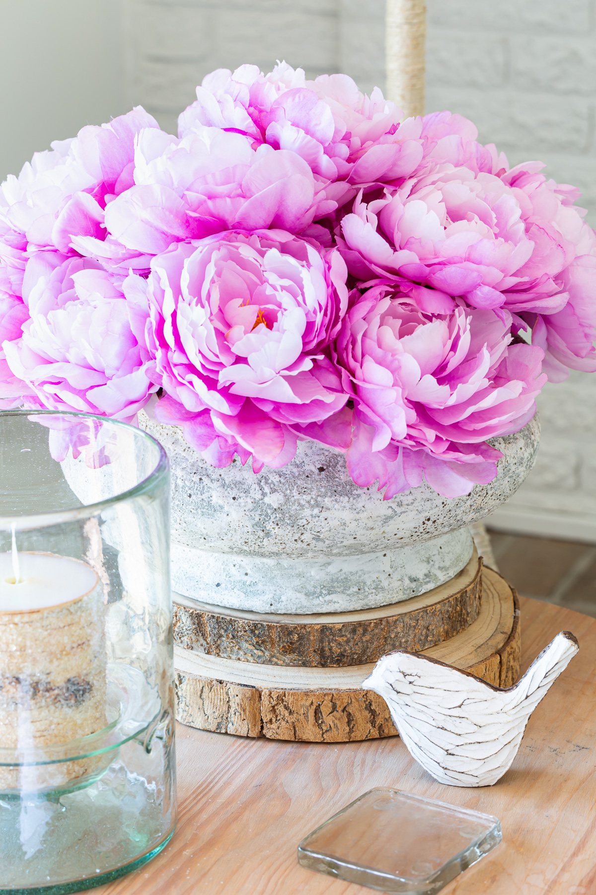 Close up of a concrete planter filled with faux pink peonies on a side table.