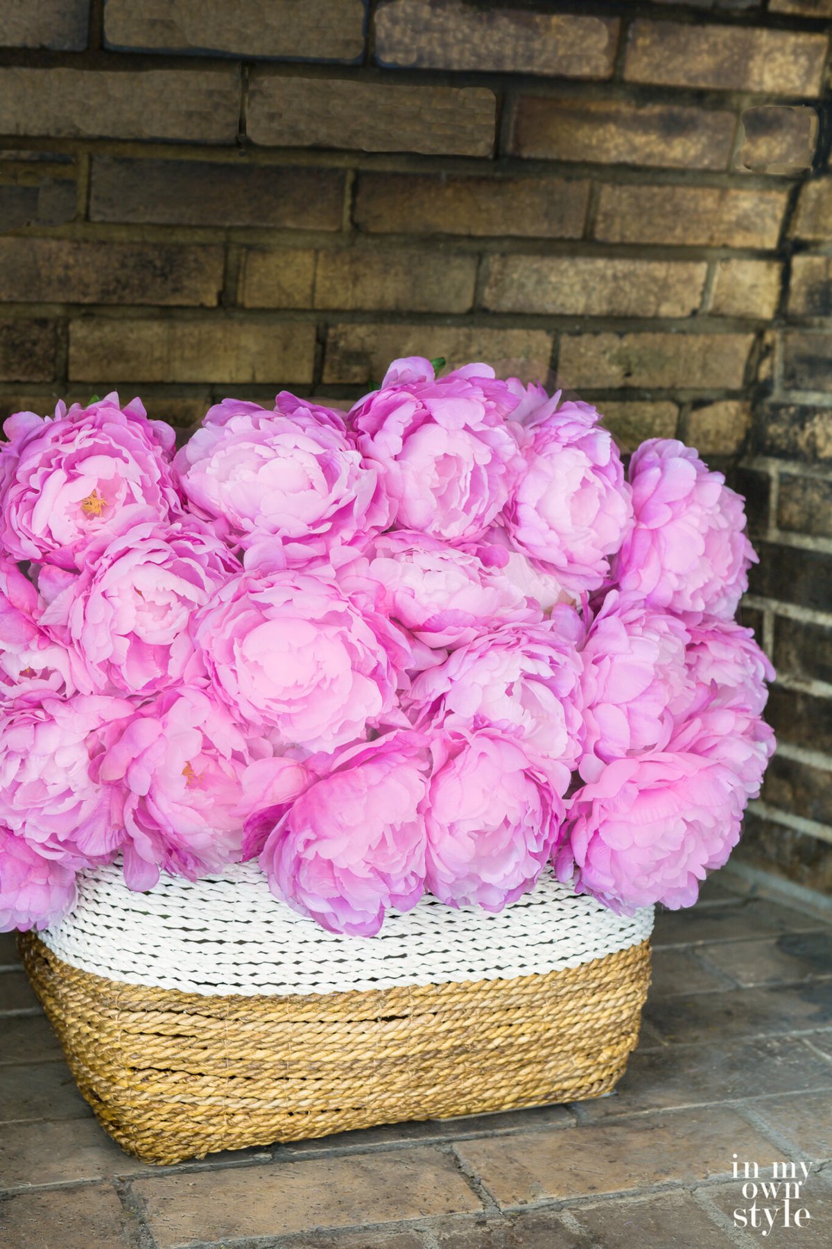 A large white and natural color basket in empty fireplace filled with pink peonies. Decorating Ideas using large baskets.