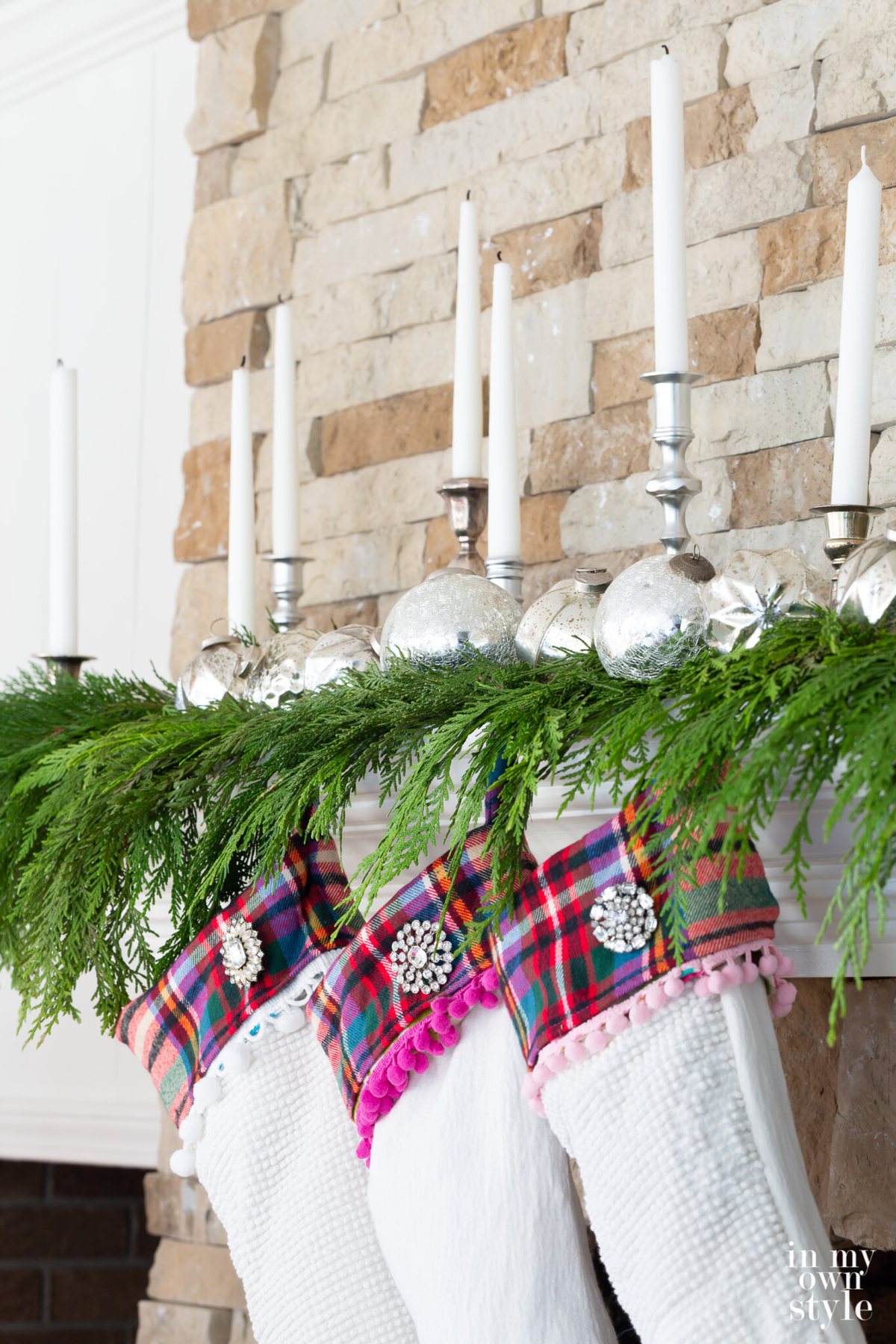 3 White Christmas stockings hanging on cedar draped fireplace mantel