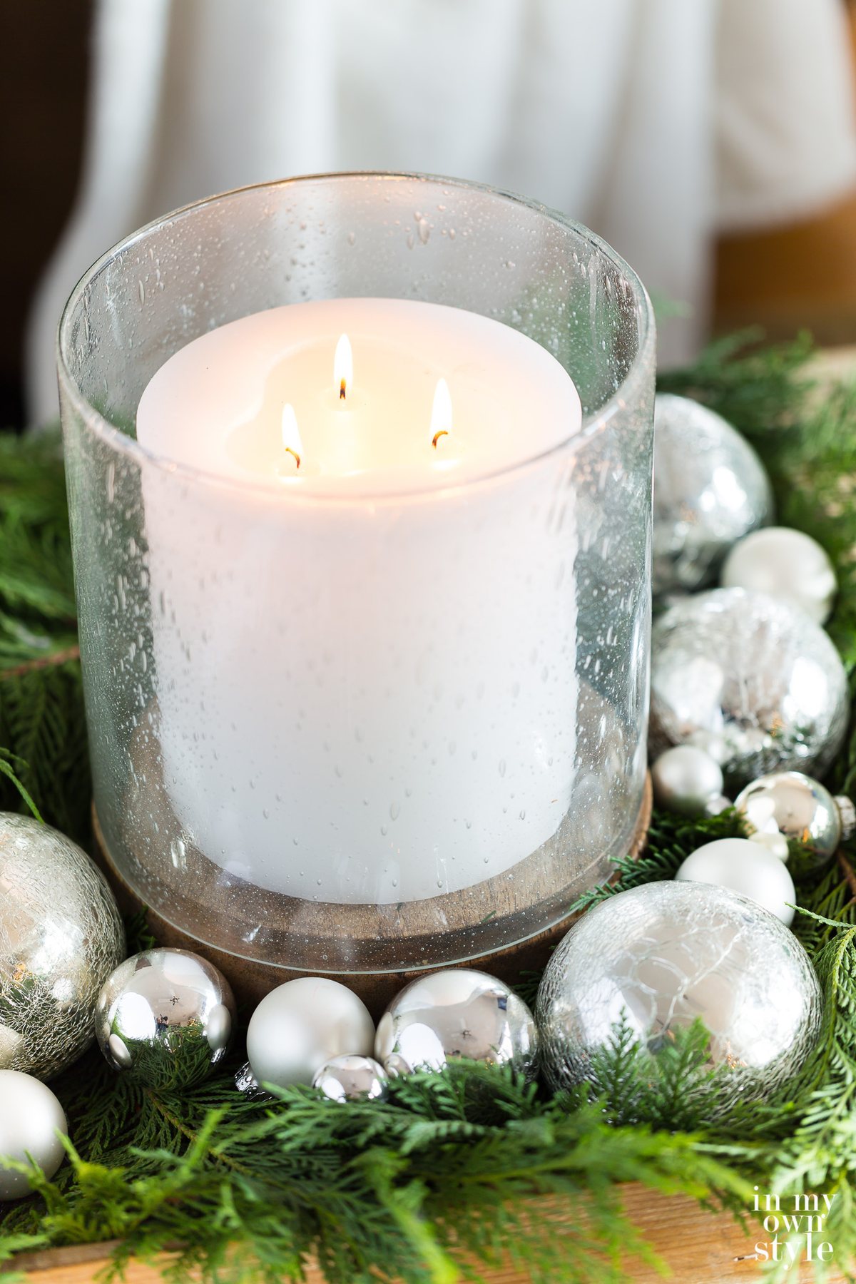 Bubble glass hurricane and large white candle table decorated for Christmas.