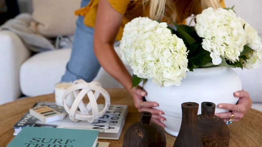Large white terra cotta vase filled with white hydrangeas from Studio McGee being placed on a coffee table