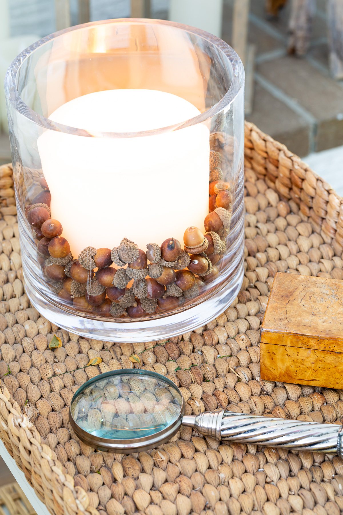 faux acorns in glass candle vase on table decorated for fall.