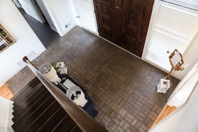Looking down from second floor of home onto a brown brick floor.