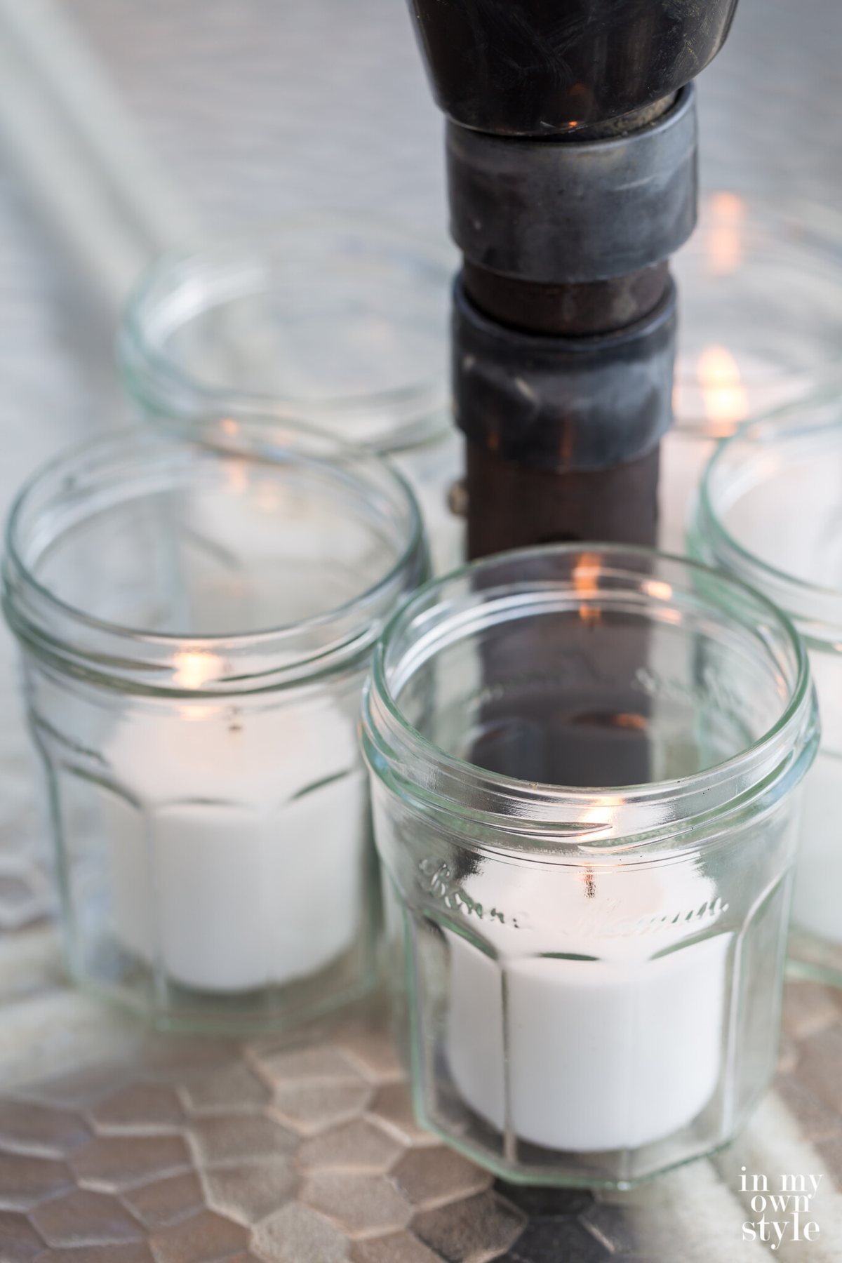 Jelly jars with candles in them around an umbrella pole on a dining table.