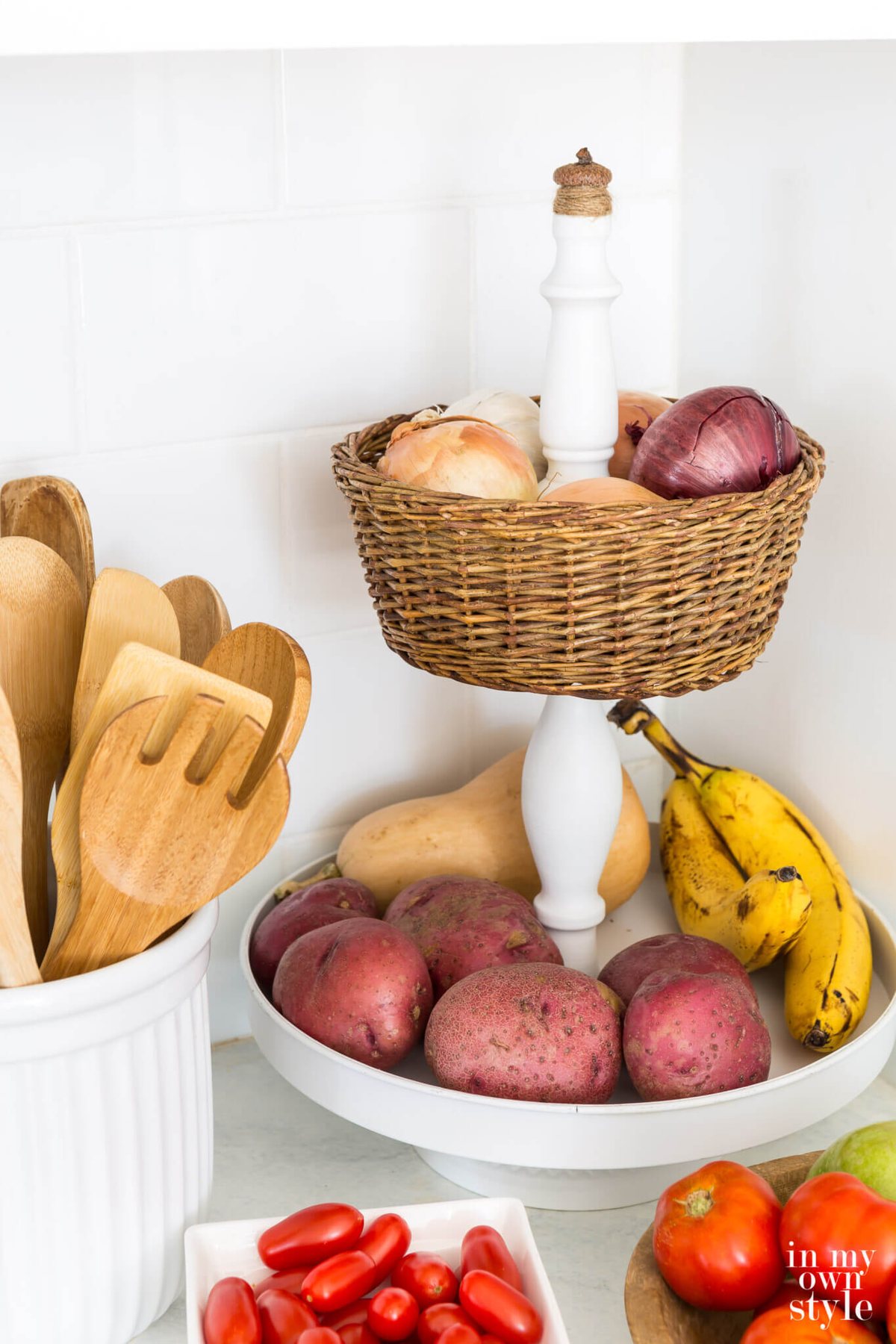 DIY tiered kitchen fruit basket using a white metal stand and a thrift store basket.