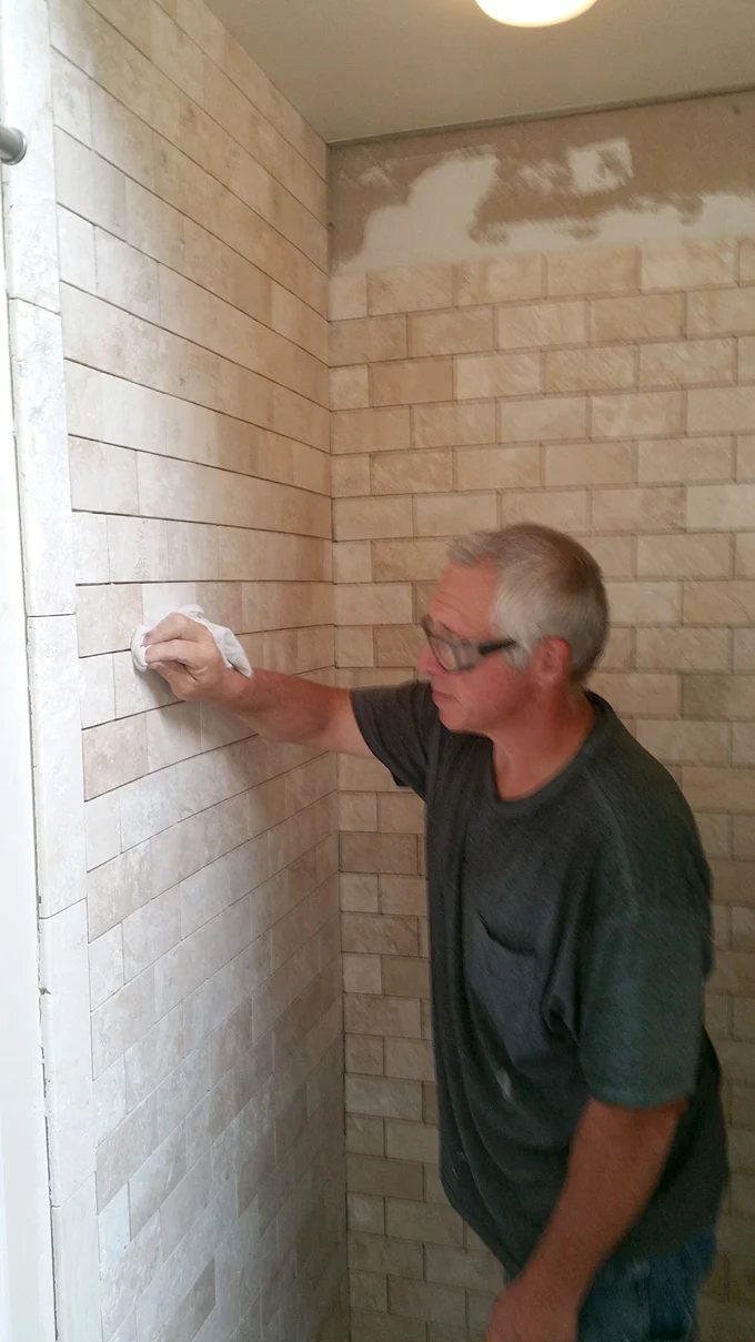 Worker standing inside shower tiling the shower walls.