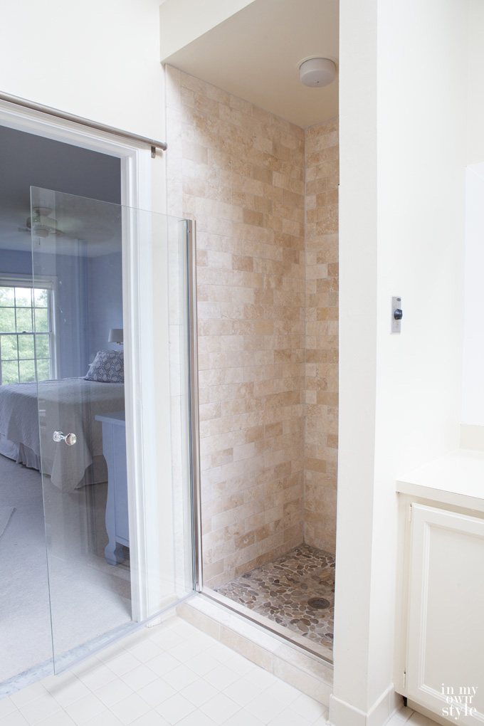 Master-bathroom-decorating showing completed tumbled stone tile makeover. Glass shower door is open.