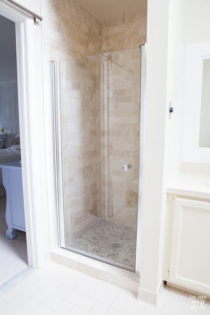 After image of new stone tile shower with clear glass door in a beige bathroom.