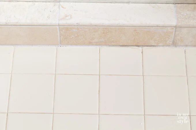 Stone-tile-shower floor next to beige tile on bathroom floor.