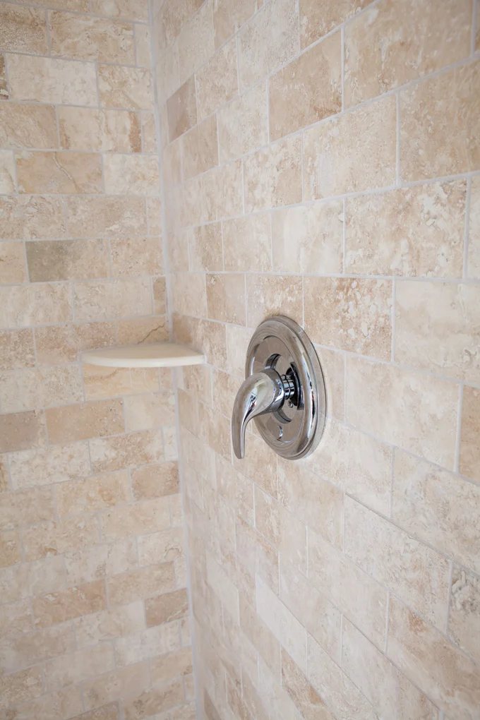 Silver shower faucet handle shown against new stone tile.