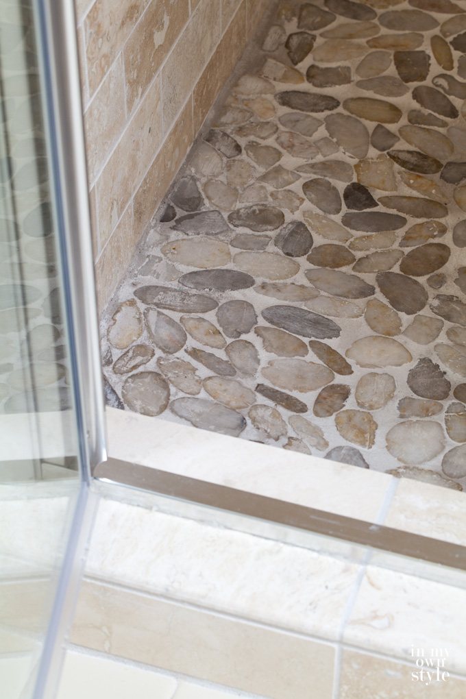 Close up of Stone-tile-shower-floor with glass door swung open.