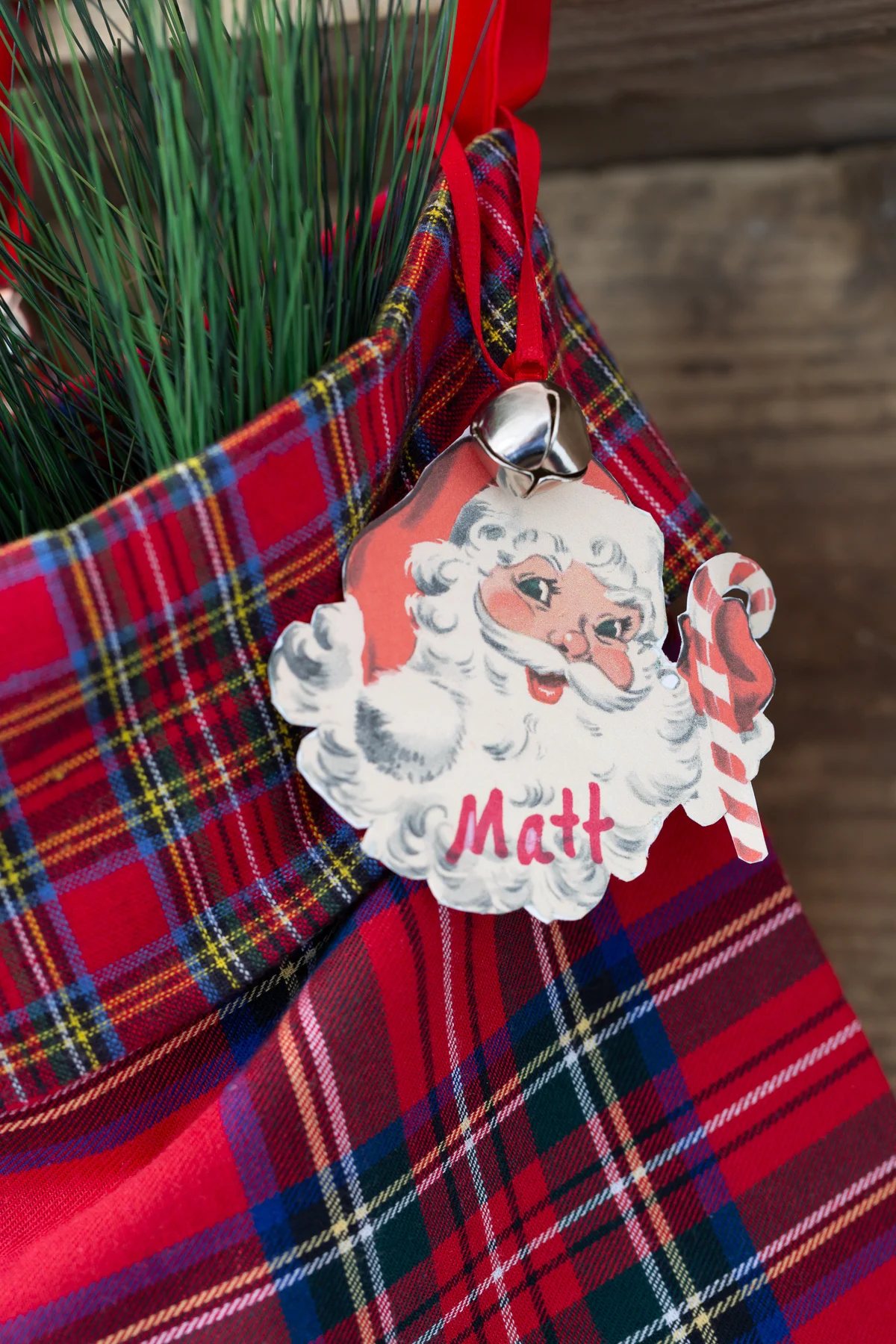 close up of a vintage Santa face tag on a red plaid stocking hanging from a mantel.