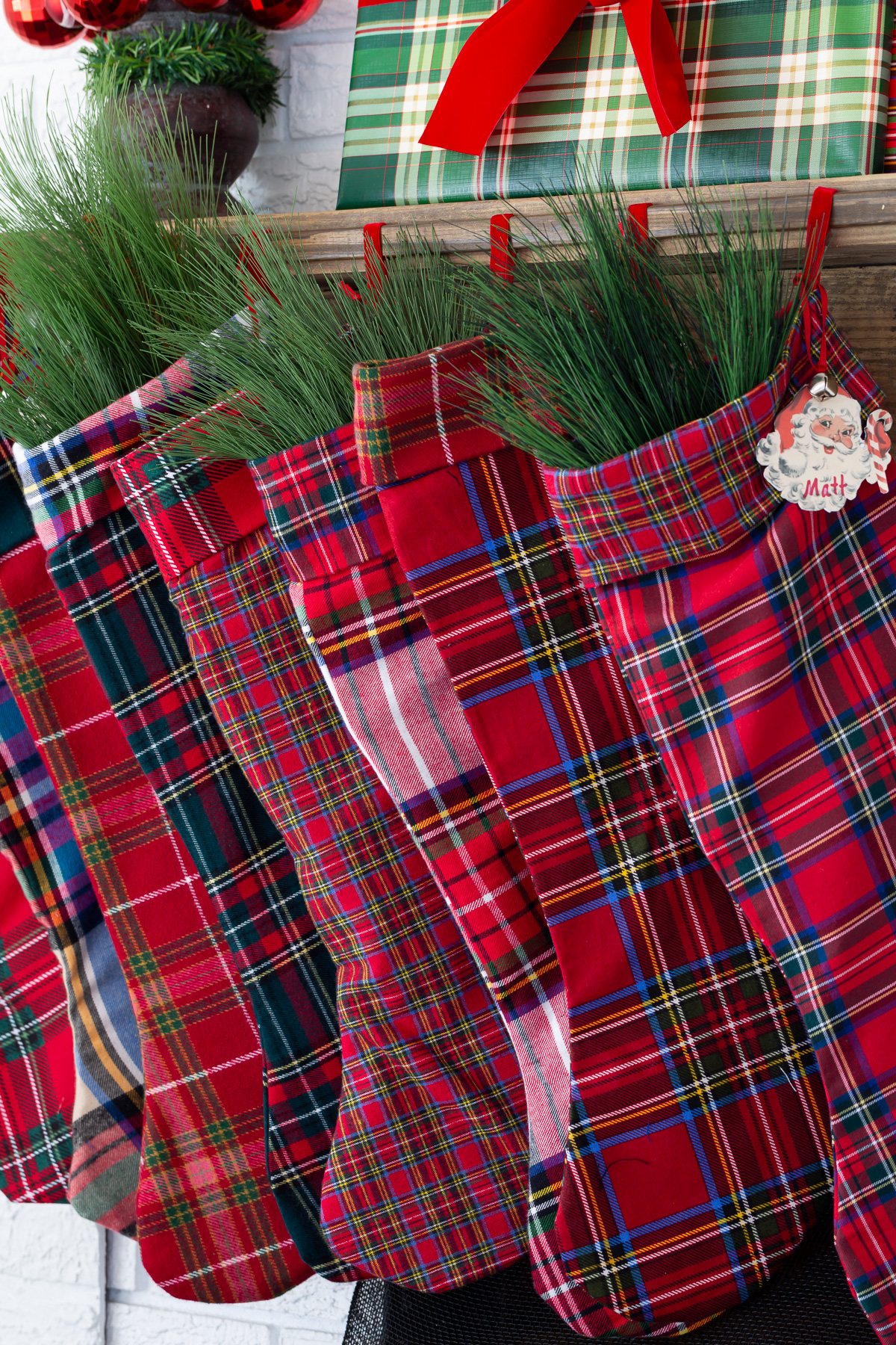 red plaid handmade stockings hanging from a wood mantel.