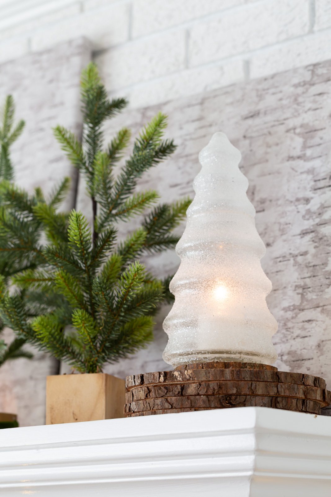 Glass and glittered Christmas tree with battery-operated candle inside on mantel.