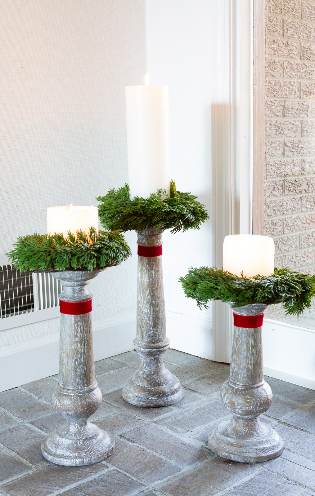 trio of large wood candle holders on floor with a wreath and red ribbon.