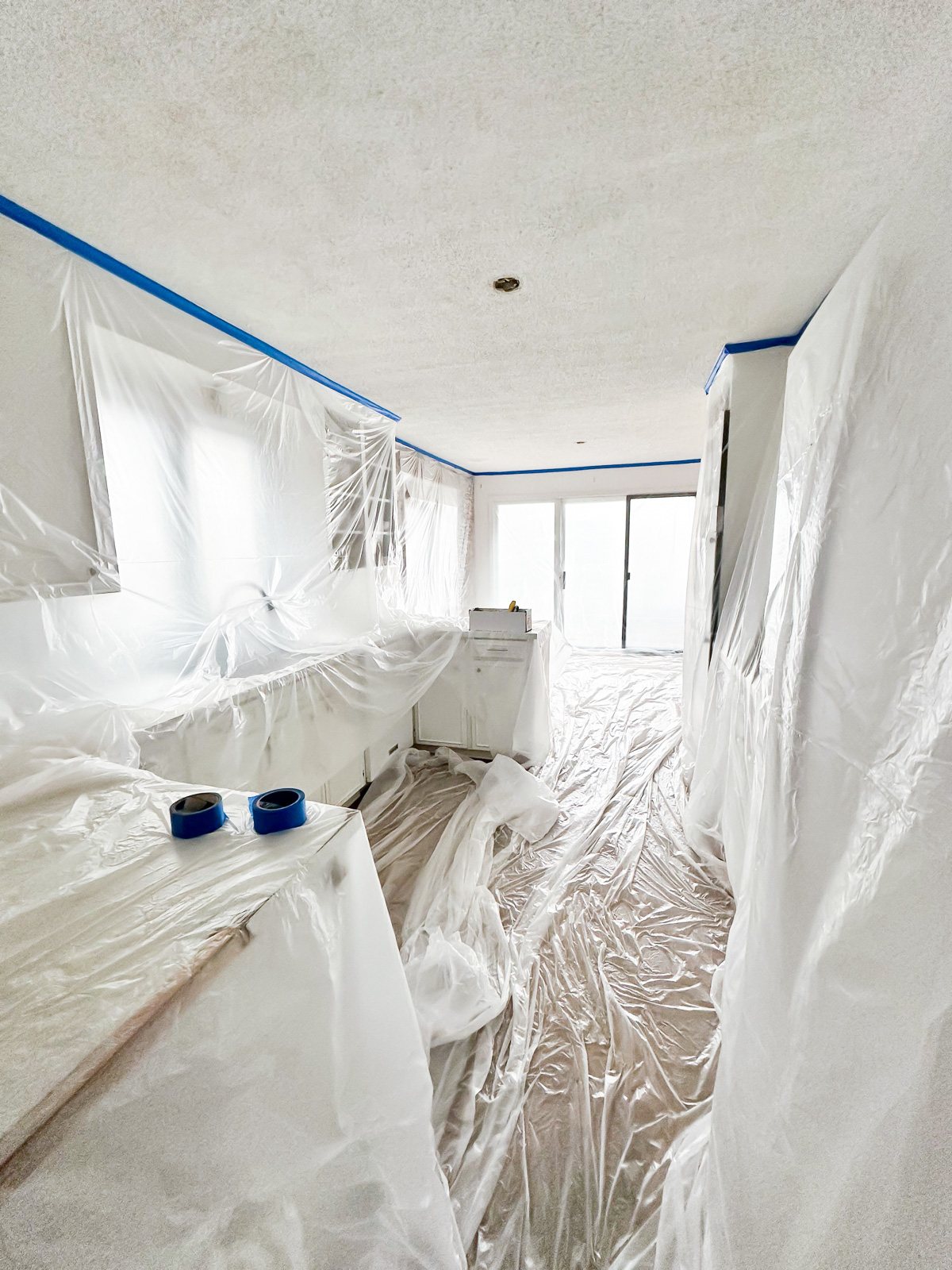 masking with plastic sheeting kitchen cabinets and floor to prepare to remove the popcorn ceiling in the room
