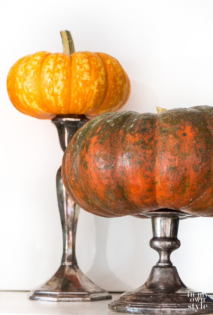 Pumpkins perched on candlestick along a fireplace mantle.