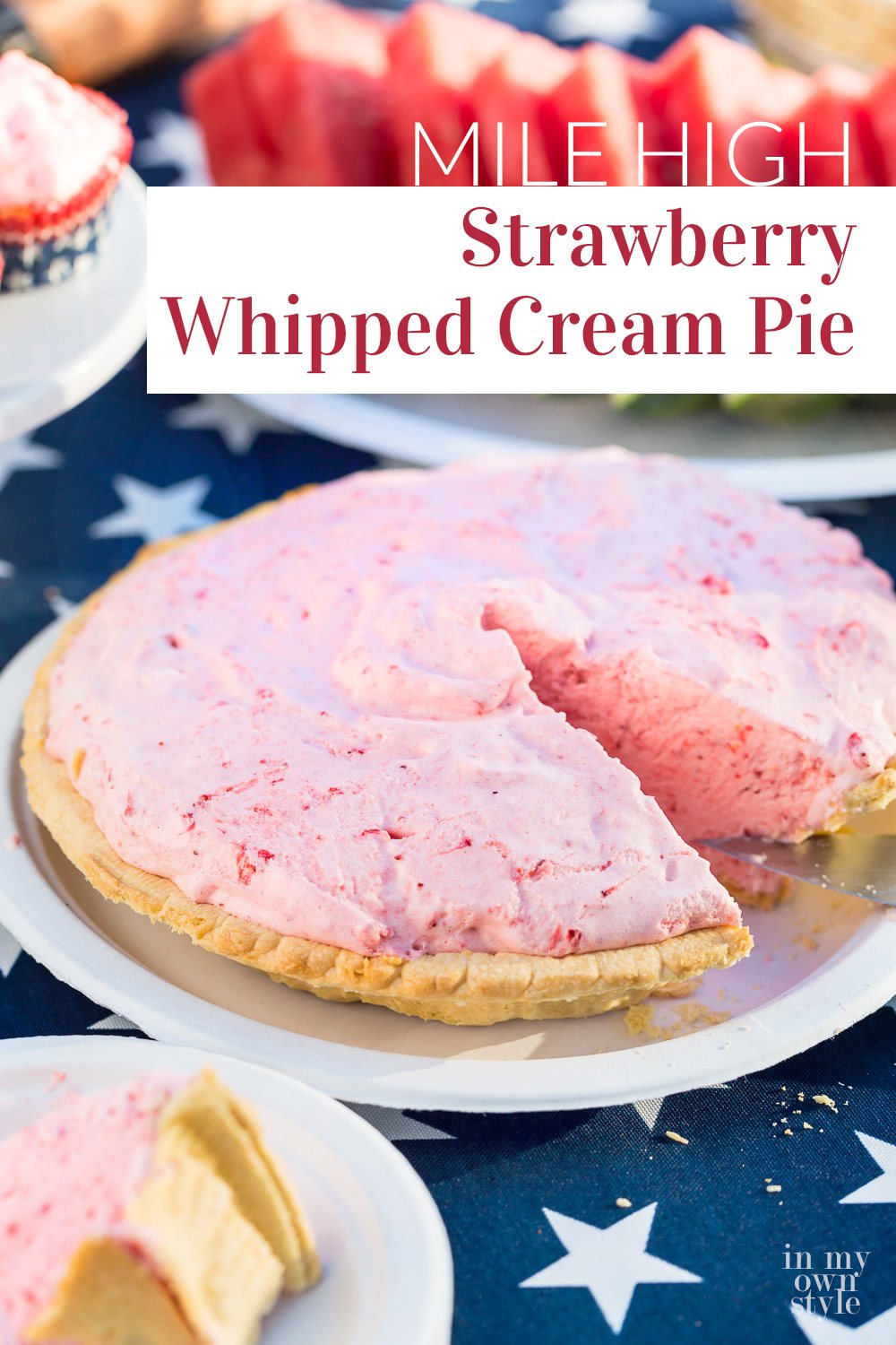 A Strawberry Whipped Cream pie with one slice cut out on a blue and white patriotic tablecloth covered picnic table.